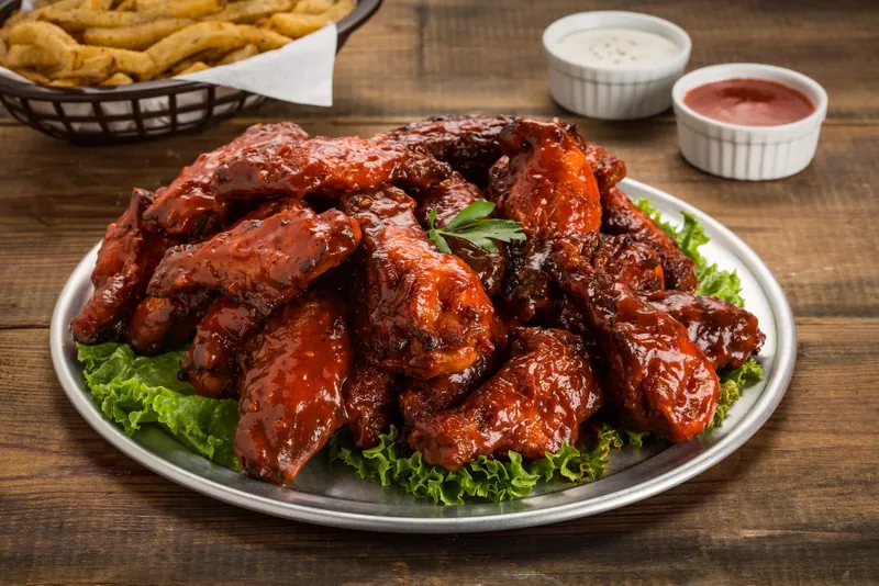 A platter of glazed chicken wings on lettuce with dipping sauces and fries